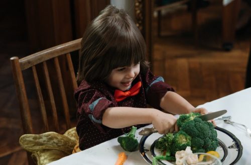 Young child excitedly cutting broccoli during a healthy meal at home.